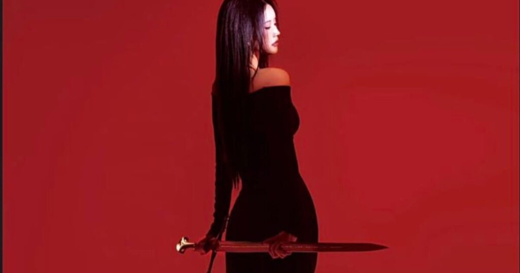 Woman in black off-shoulder dress holding a sword against a red background, dark feminine energy