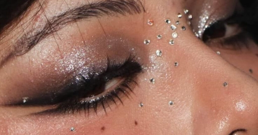 Close-up of a woman's eye with glitter and crystal gems, editorial dark feminine beauty look