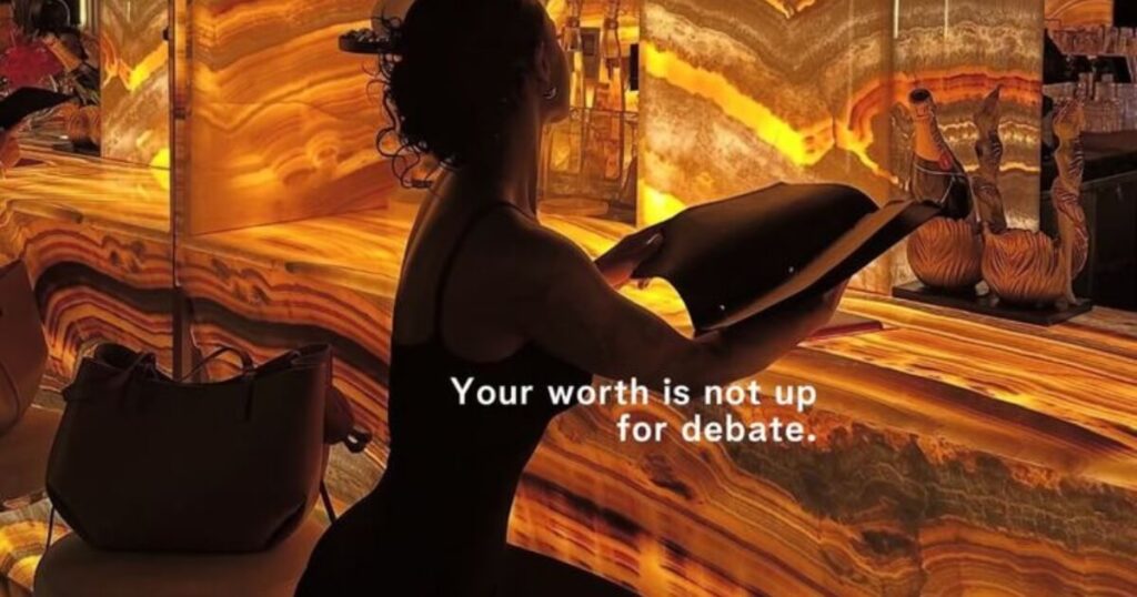Silhouette of a woman reading in an amber-lit room with the text "Your worth is not up for debate