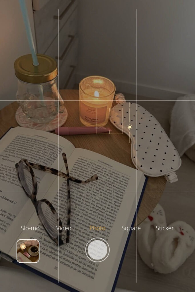Flat lay of a book, candle, journal, and sleeping mask arranged on a soft surface in gentle lighting.