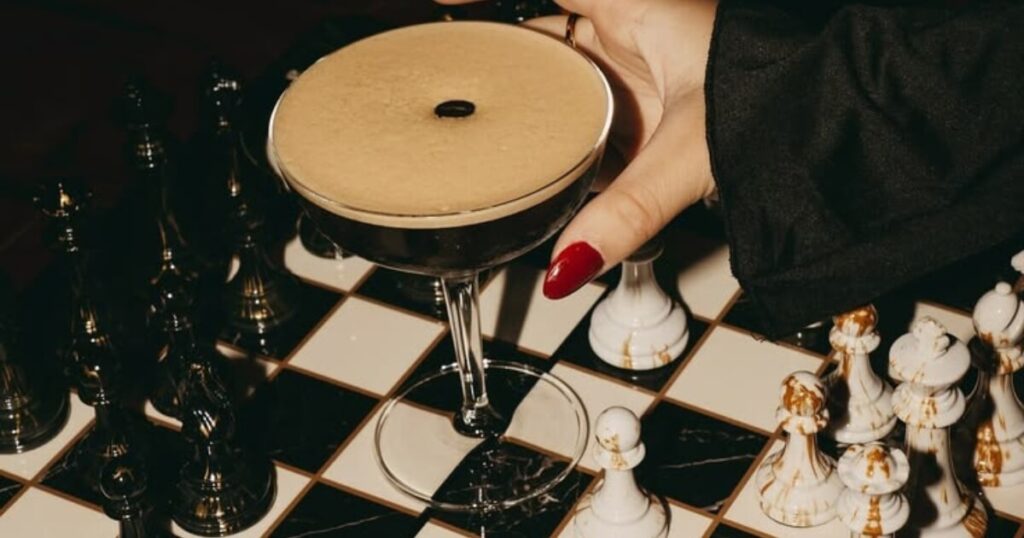 Woman holding espresso martini over a chess board — dark feminine aesthetic