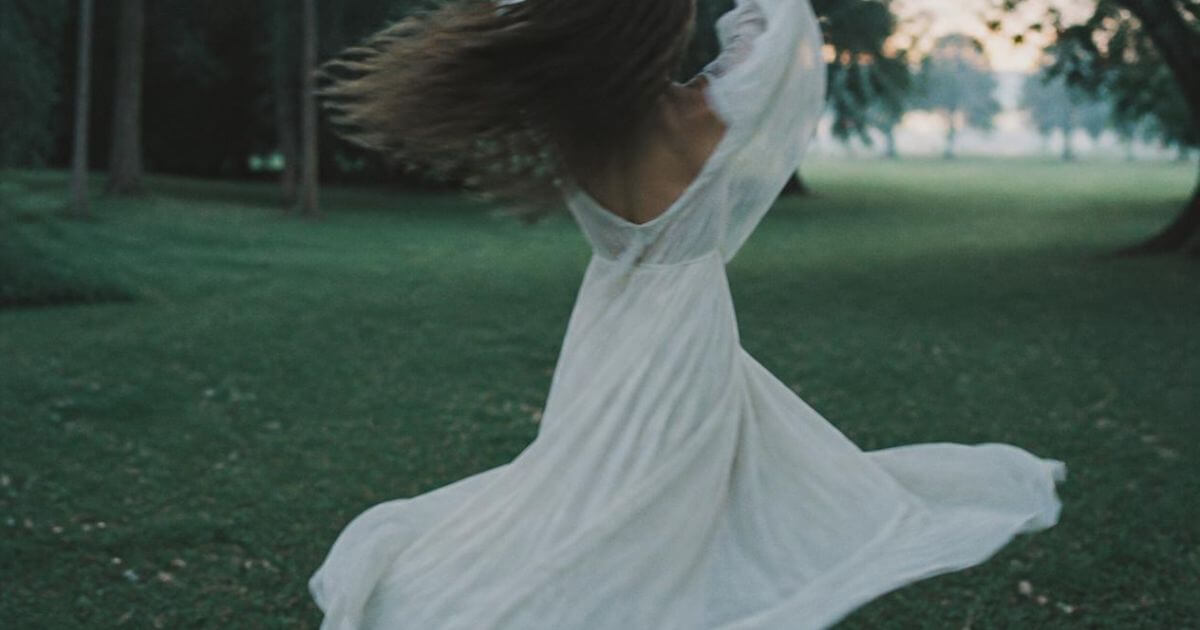 Woman twirling in white dress on a lawn, freedom and softness