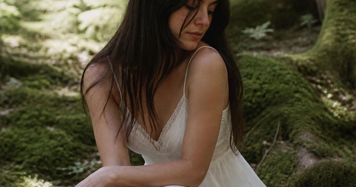 Woman sitting quietly in a mossy forest clearing, soft feminine era