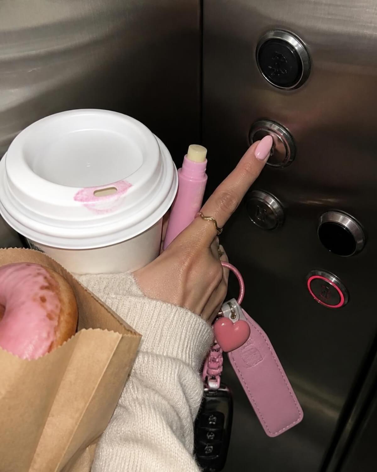Hand holding a takeaway coffee, lip balm and a bakery bag in an elevator, the small daily purchases that stop you from spending money wisely