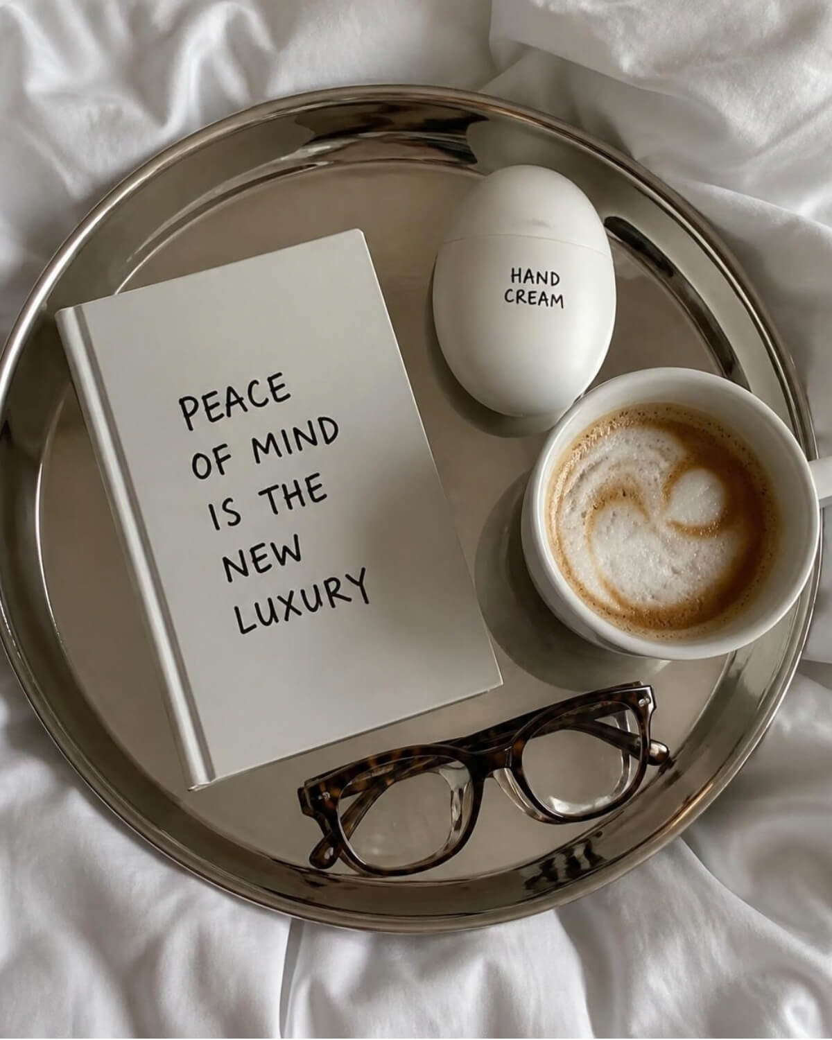 Notebook reading peace of mind is the new luxury on a silver tray with coffee and glasses, a symbol of a positive money mindset