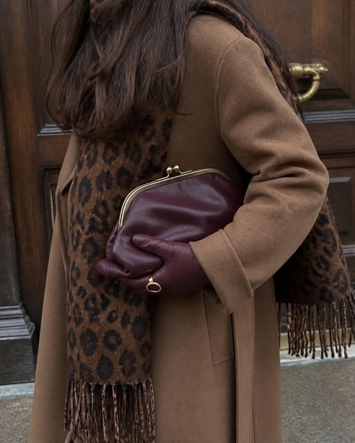 Woman in a camel coat, leopard scarf and burgundy gloves holding a leather clutch, timeless evergreen pieces that help you spend less