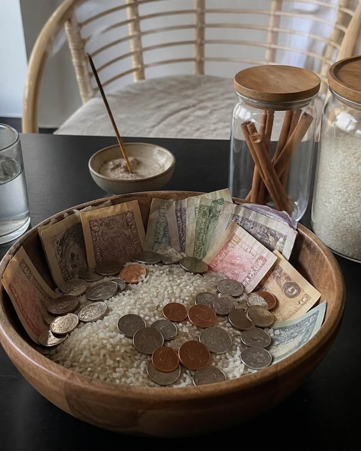 Wooden money bowl with rice, coins and banknotes on a table, a symbolic savings ritual that makes saving money a habit