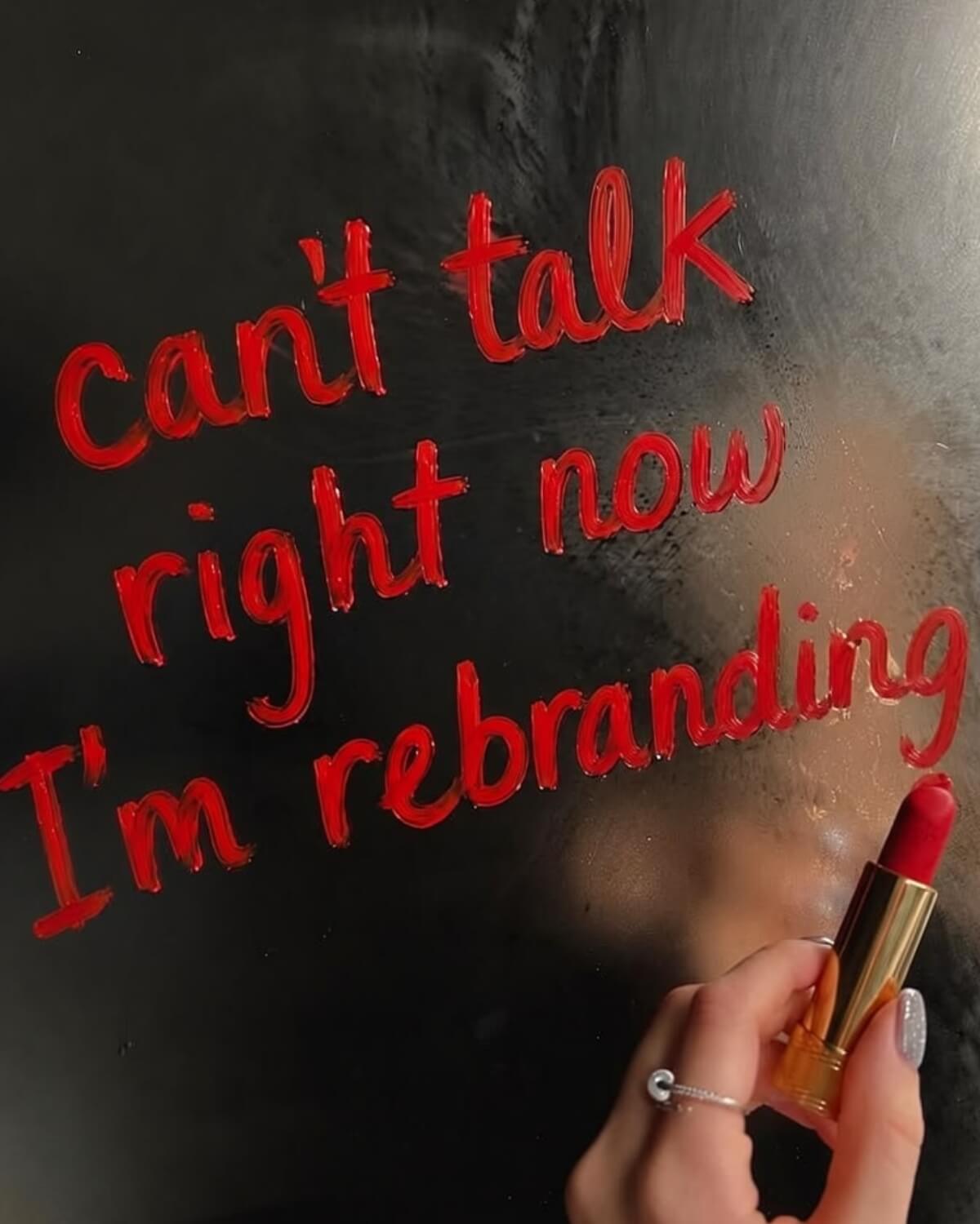 Hand writing can't talk right now I'm rebranding in red lipstick on a dark mirror, a playful symbol of acting from your future self identity