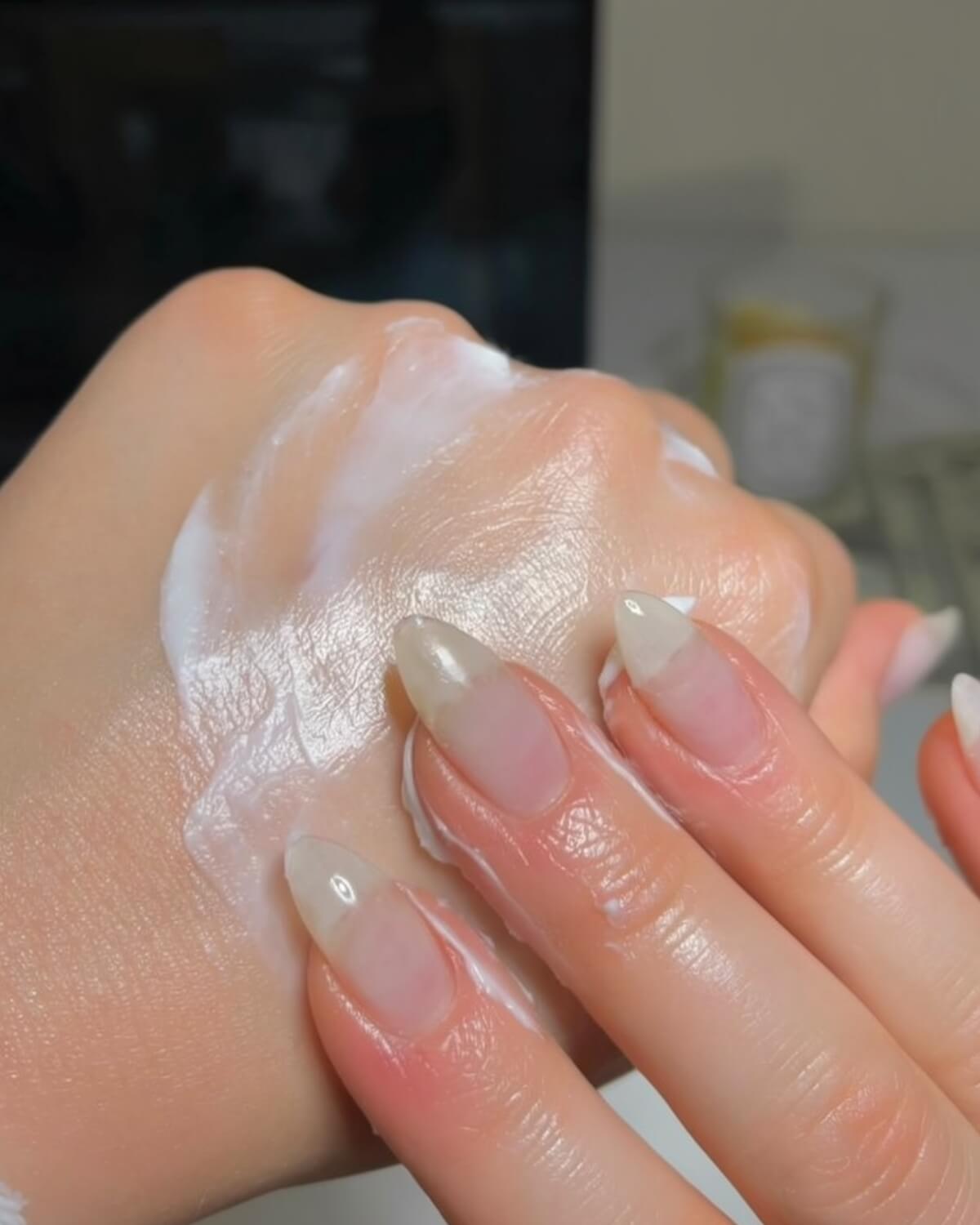 Close-up of hands with almond nails massaging thick white hand cream, a simple hand care step in the 30 day glow up challenge