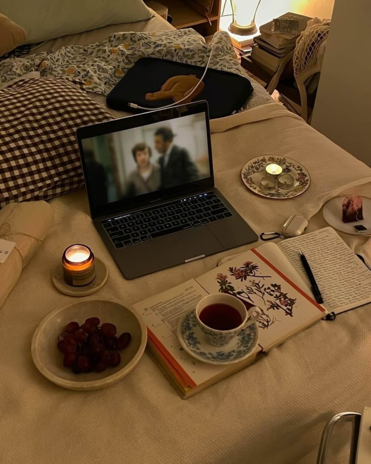 Cozy bed with tea, candles, a journal, a botanical book and grapes on a knit blanket, an intentional evening wind-down ritual