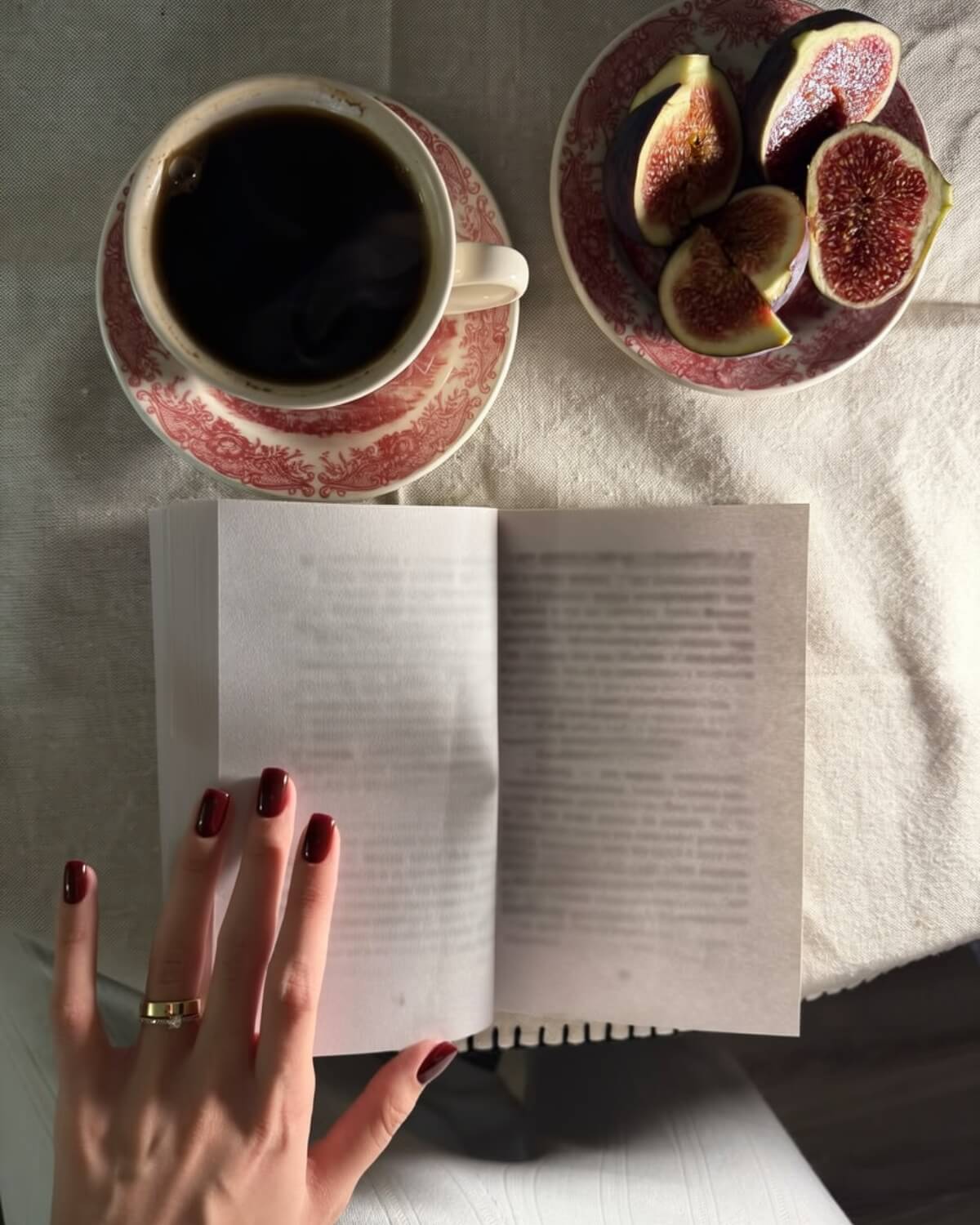 Black coffee in a red and white porcelain cup, fresh figs and an open book with a hand resting on the page, an intentional morning as a daily anchor to your future self
