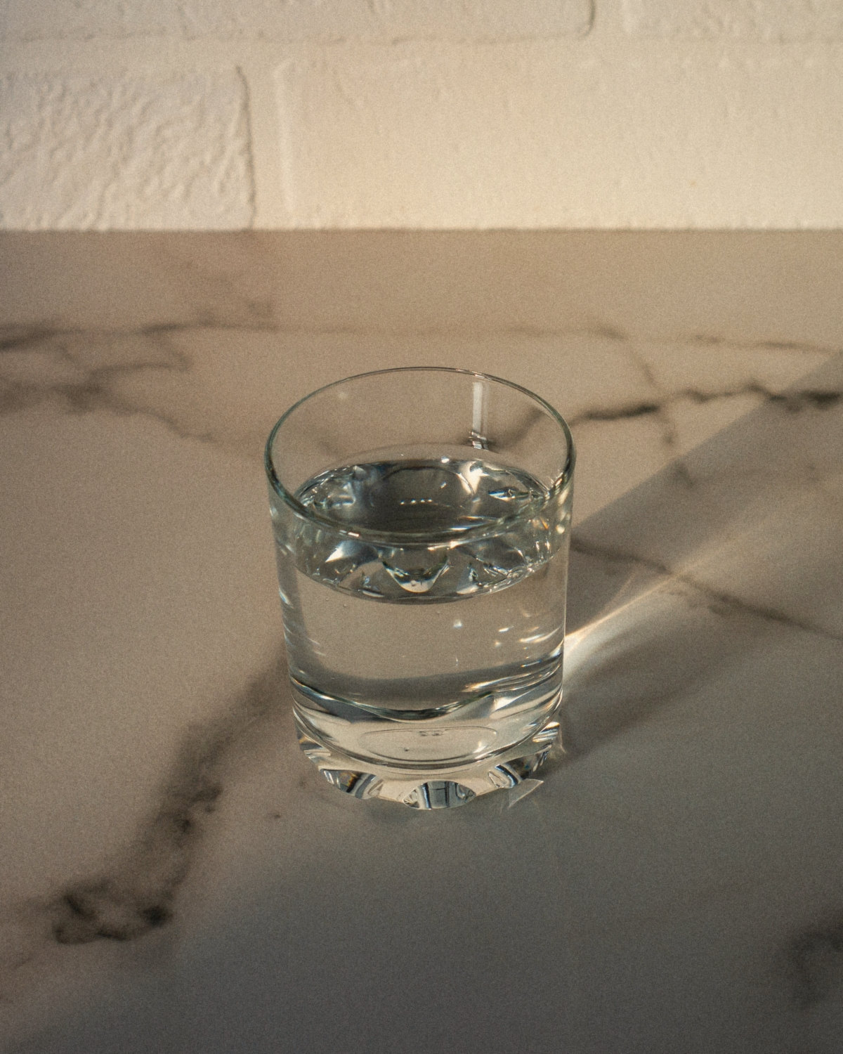 A simple glass of water on a marble table in soft afternoon light, a small gesture of trust before a confident conversation