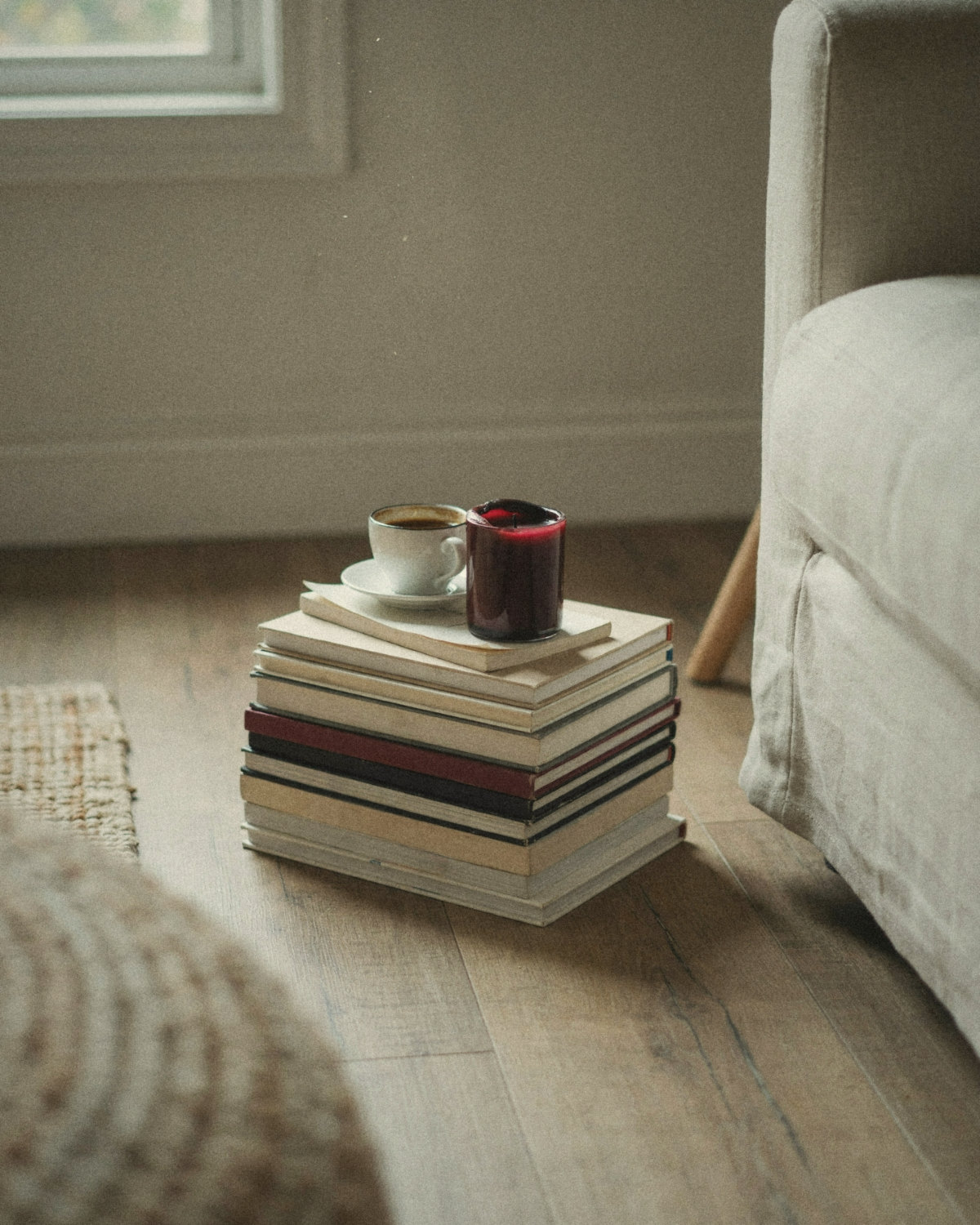 Stack of books with an espresso cup and a burgundy candle beside a linen sofa, reading about confident communication and people skills