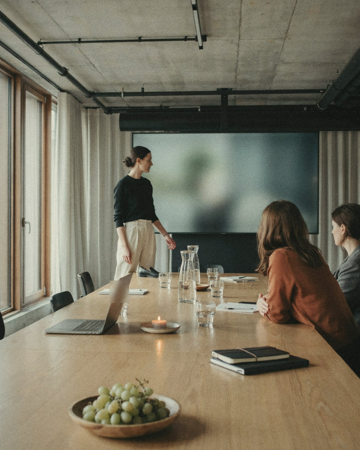 Woman in a black top presenting calmly at the head of a long meeting table while colleagues listen, good communication skills at work
