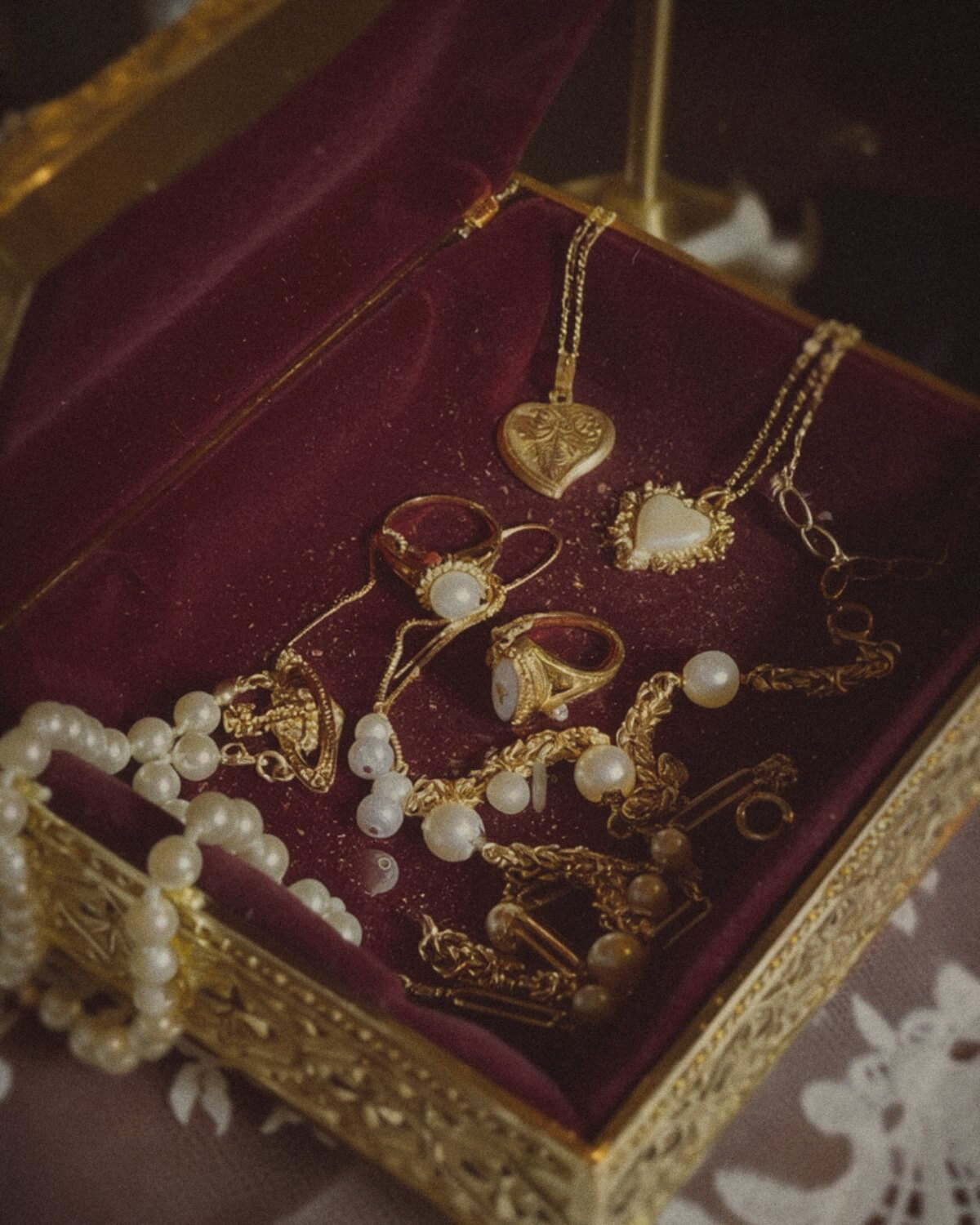 Antique gold filigree jewelry box lined with burgundy velvet holding gold heart lockets, rings and pearls, dark feminine accessories
