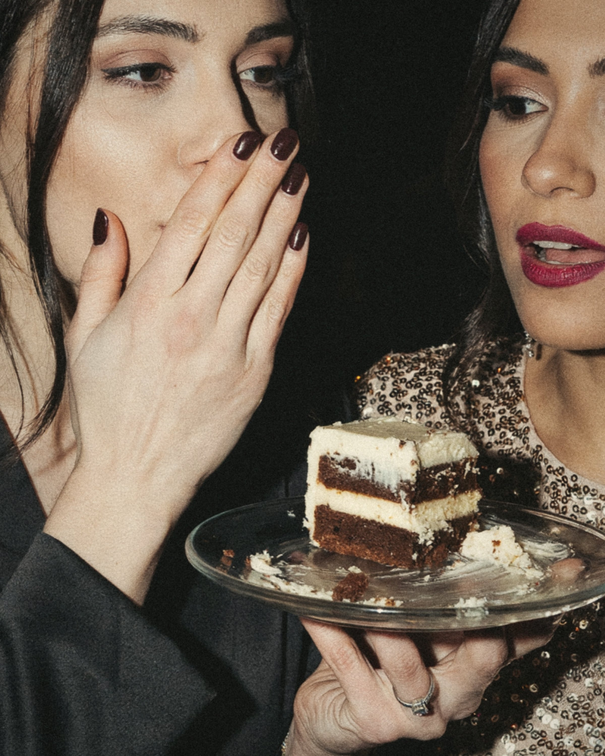 Two women at a party leaning close, one whispering and the other listening intently over a slice of cake, the art of listening