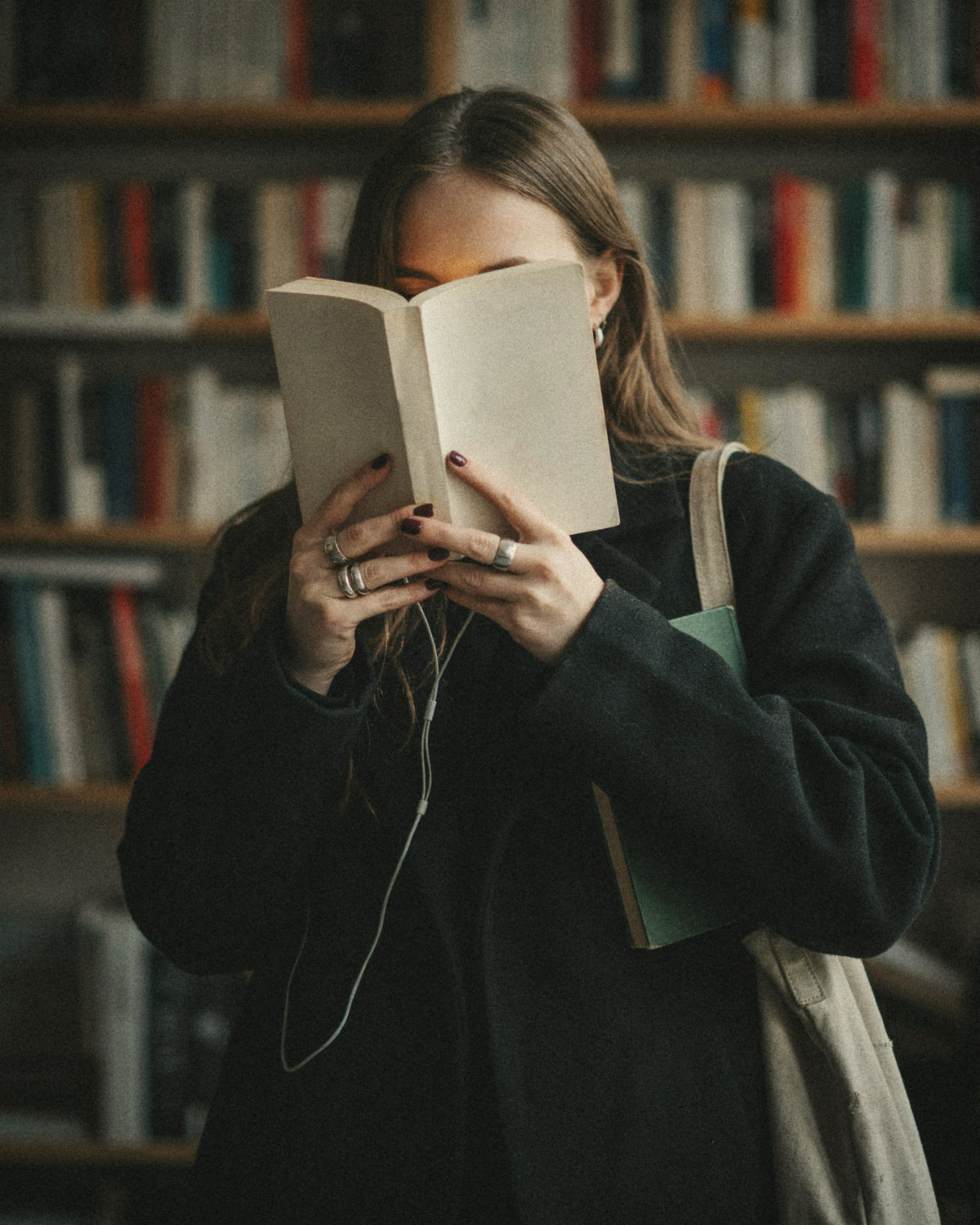 Woman in a black coat with burgundy nails reading a book in a bookshop, learning people skills for social networking