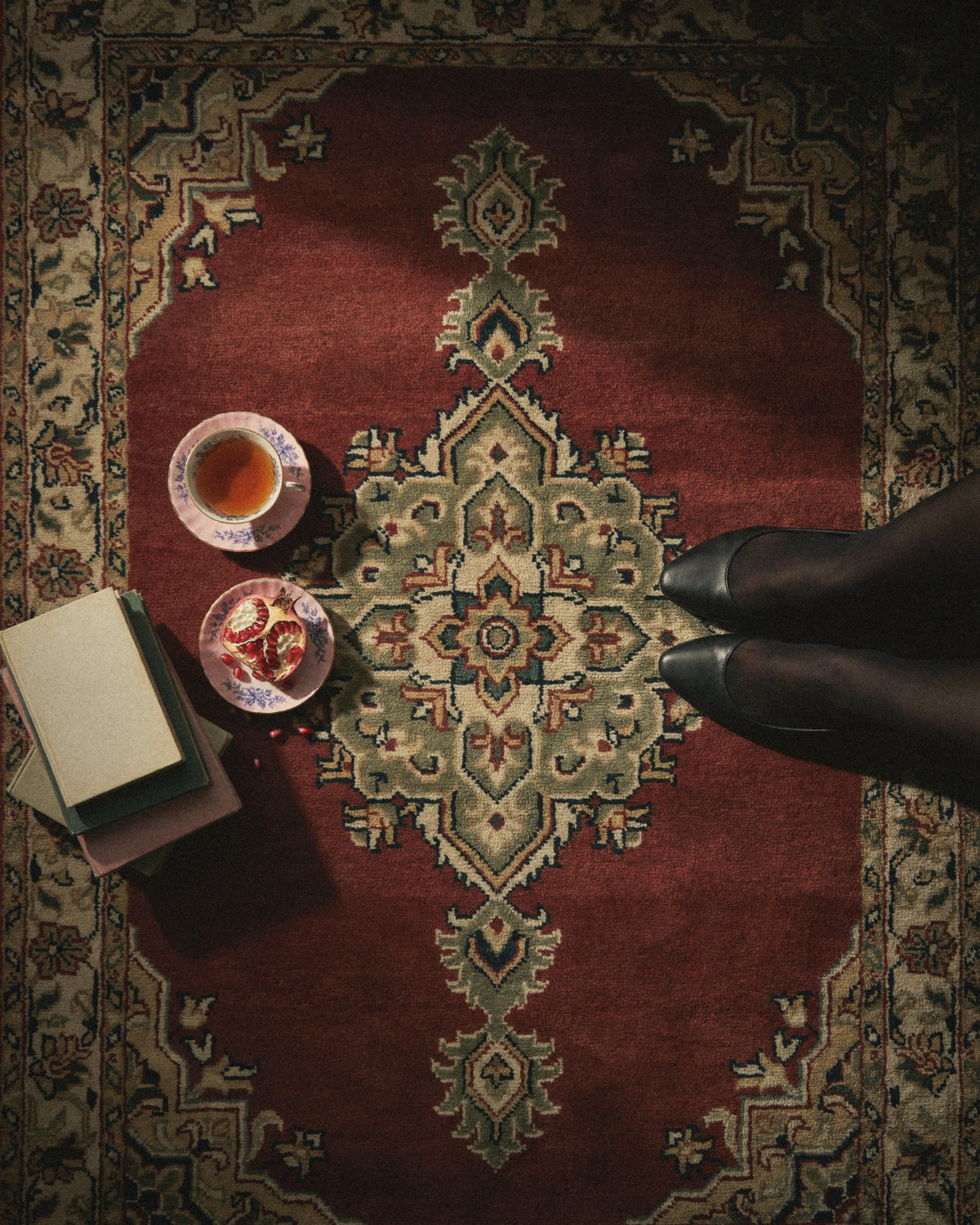 Overhead view of a red patterned rug with books, a teacup and a halved pomegranate next to black pointed flats, finding your personal brand topics