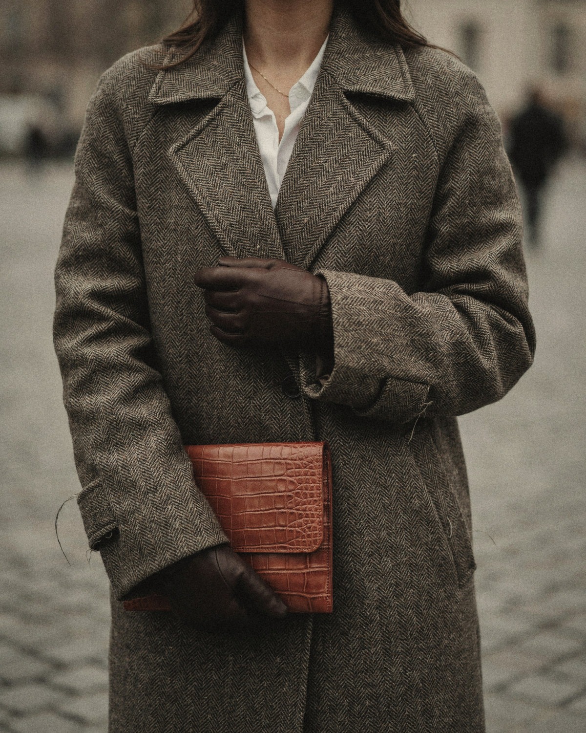 Woman in a herringbone wool coat and brown leather gloves holding a croc-embossed clutch, the signature details of consistent self branding